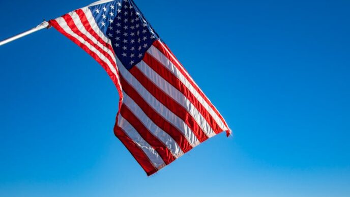 The American flag proudly waves on a flagpole against a clear blue sky, symbolizing freedom and patriotism.