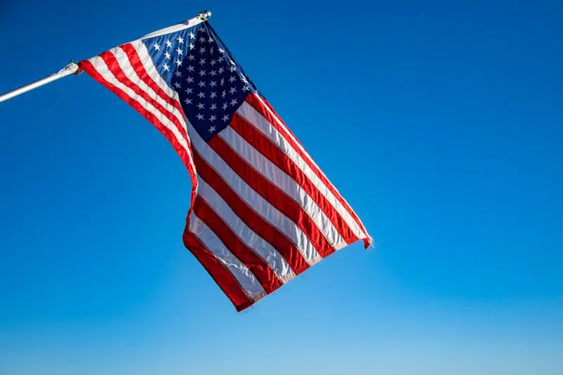 The American flag proudly waves on a flagpole against a clear blue sky, symbolizing freedom and patriotism.